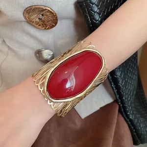 Close-up view of a vintage gold hollow-out cuff bracelet featuring a large red oval resin stone