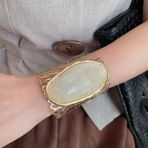 Detailed view of an oversized hollow gold cuff bracelet with a large oval cream stone center