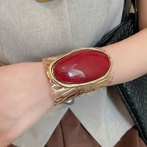 Close-up of vintage hollow-out gold cuff bracelet with large red oval resin stone