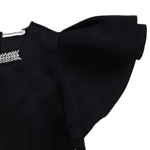 Detail showing crew neck with leaf-shaped rhinestone and flutter sleeves on a black dress
