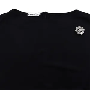 Dettaglio dello scollo di un abito nero elegante con spilla a fiore e etichetta brand