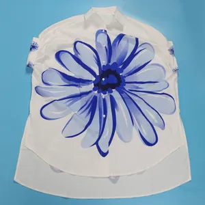 Detail van elegant wit asymmetrisch shirt met blauwe bloemenprint en reverskraag.