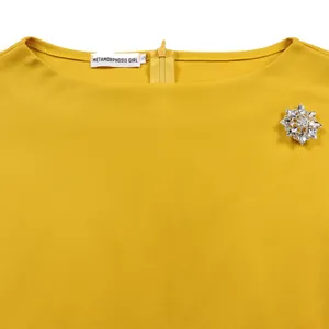 Dettaglio dello scollo di un abito giallo con una spilla a forma di fiore di cristallo
