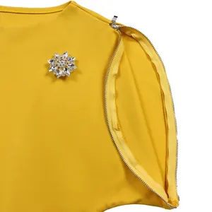 Dettaglio dell'abito giallo con spilla a fiore di strass e cerniera decorativa sulla spalla