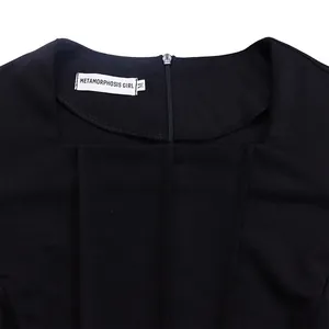 Close-up of square neckline and METAMORPHOSIS GIRL brand label on an elegant black dress.
