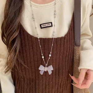 Primo piano di una collana con fiocco a pois bianchi e neri su un maglione crema.