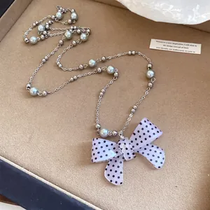 Primo piano del ciondolo a fiocco in acrilico a pois su catena di perle argentate.
