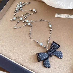 Primo piano della collana con fiocco a pois bianchi e neri, perle e ciondolo in acrilico.