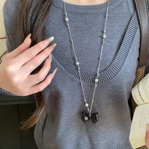 Dettaglio di una collana con fiocco nero a pois bianchi indossata su un maglione grigio.