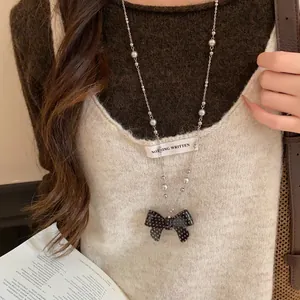 Primo piano della collana con fiocco nero a pois e perle su un maglione beige dolce.