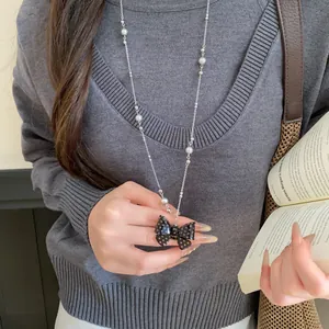 Dettaglio di una collana con fiocco a pois neri abbinata a un maglione grigio e libro
