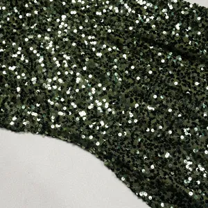 Macro detail of dark green sequin fabric with mesh backing for elegant evening dress
