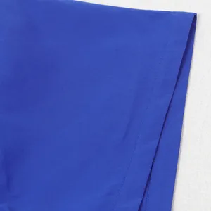 Detailaufnahme der blauen Stofftextur und der präzisen Nähte am Saum eines Jumpsuits.