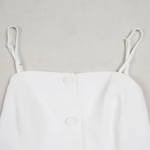 Détail d'une combinaison blanche à fines bretelles avec boutons recouverts de tissu devant