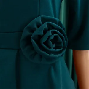Detailaufnahme eines smaragdgrünen Kleides mit handgefertigter 3D-Stoffblume an der Taille.