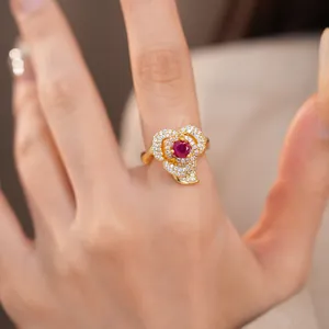 Close-up view of an elegant 14k gold plated flower ring with red zircon on a finger.