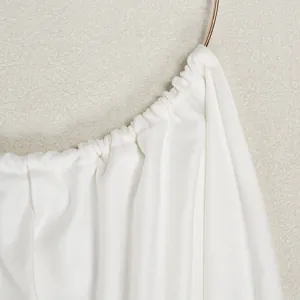 Close-up detail of white pleated fabric gathered at a golden metal ring neckline attachment.