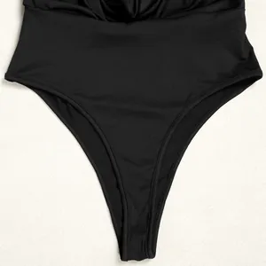Close-up of black pleated swimsuit fabric and high-cut leg detail on textured background