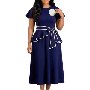 Elegant detail of navy blue dress with white floral brooch and peplum waist tie.