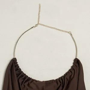 Detail of gold metal halter neckline with adjustable chain on brown pleated top