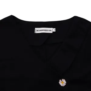 Close-up of black casual V-neck top featuring brand label and a delicate white daisy flower pin