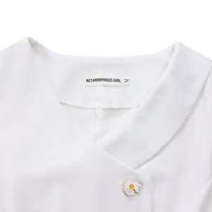Close-up of white V-neck top neckline with elegant daisy button and brand label.