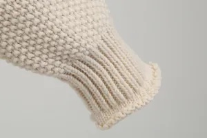 Close-up macro detail of the ribbed cuff on a chunky cream-white knit sweater pullover.