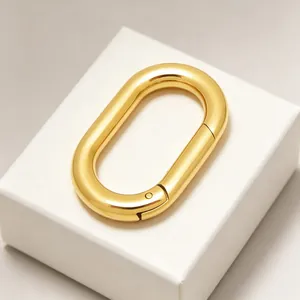 Vue macro d'un fermoir à ressort ovale doré de luxe sur un socle blanc minimaliste.