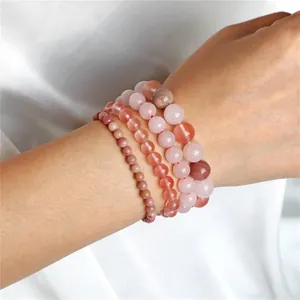 Detail shot of stacked natural pink quartz and rhodonite stone beaded bracelets on wrist.