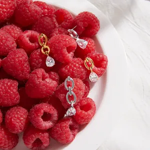 Detail of teardrop zircon earrings with links set against fresh red raspberries.