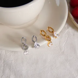 Close-up detail of luxury gold and silver teardrop zircon link earrings on a white ceramic cup.