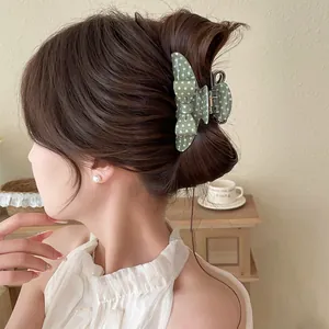 Close-up view of an elegant green polka-dot bow hair claw clip styled in a modern updo