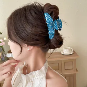 Detailed view of a stylish blue polka dot bow hair claw clip on a dark brown hair bun