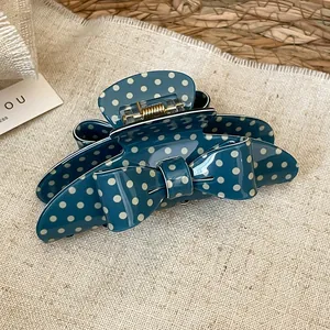 Detailed view of the teal acrylic polka dot bow hair claw clip with metal spring.
