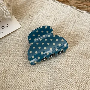 Detail view of a blue acrylic hair claw clip with white polka dots and elegant bow design
