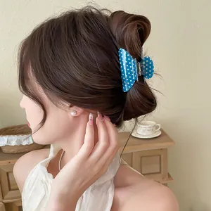 Blue polka dot bow hair claw clip made of acrylic shown on a bun for hair styling