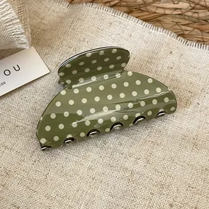 Detail of green acrylic shark hair claw clip with retro white polka dot pattern.