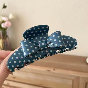 Detail view of a blue acrylic hair claw clip with white polka dots and a bow design.