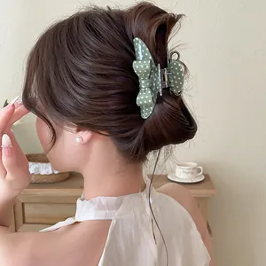 Detailed view of an elegant green polka dot bow hair claw clip on a stylish bun hairstyle