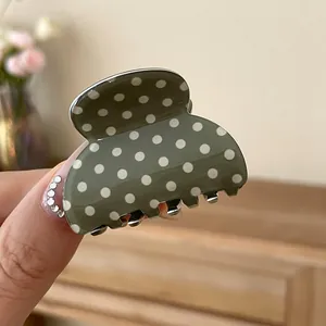Close-up view of an elegant green acrylic hair claw clip with a white polka dot pattern
