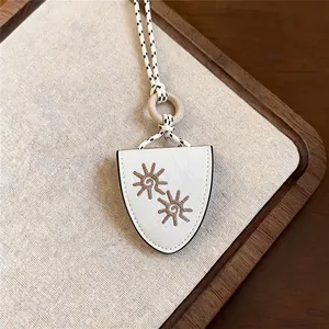 Close-up of white leather shield-shaped pendant with intricate sun embroidery details