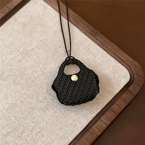 Detailed view of a retro black woven leather pouch pendant necklace on fabric background
