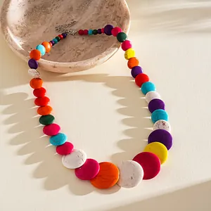 Detailed view of a vibrant multi-color graduated acrylic bead necklace on a beige stone plate