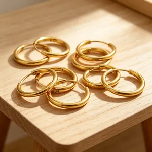 Close-up detail of minimalist gold-finished stainless steel hoop earrings on a wooden surface