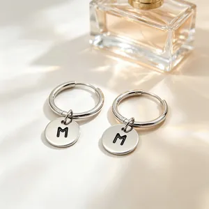 Close-up of silver stainless steel hoop earrings with an engraved initial M pendant.