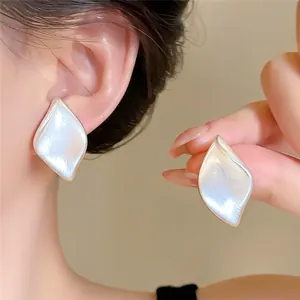 Gros plan de boucles d'oreilles élégantes en forme de feuille d'argent mat au style épuré.