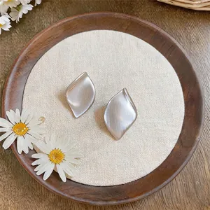 Gros plan de boucles d'oreilles en forme de feuille d'argent mat sur un plateau en bois rustique