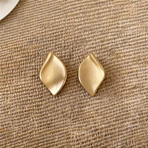 Gros plan sur d'élégantes boucles d'oreilles feuilles en or mat sur fond de tissu tissé