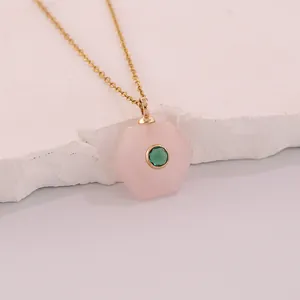 Close-up of a hexagonal pink natural stone pendant with a green inlaid gem on gold chain.
