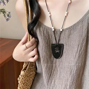Close-up of a stylish pearl necklace with a black pouch pendant and bear charm detail